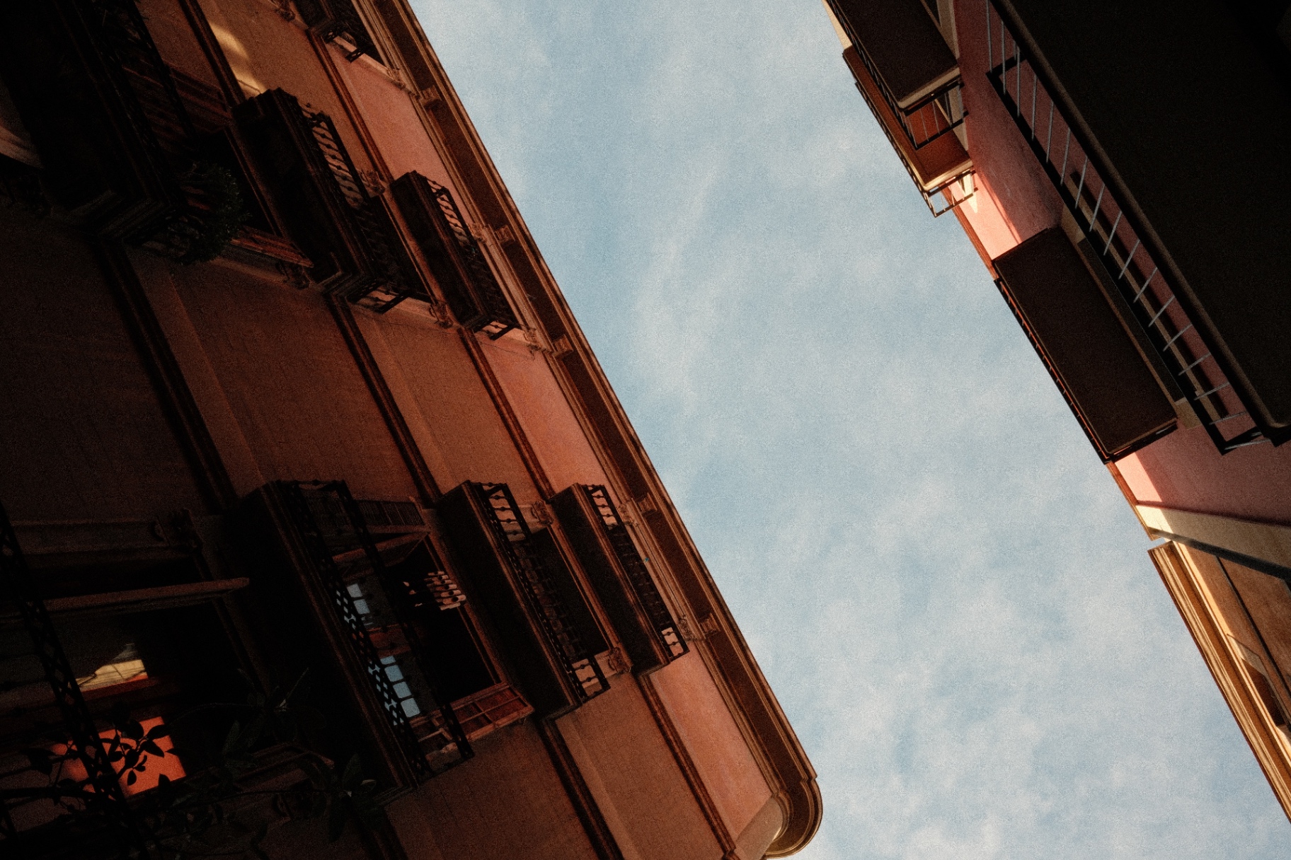 Looking up between two ochre and pink facades to a soft blue sky