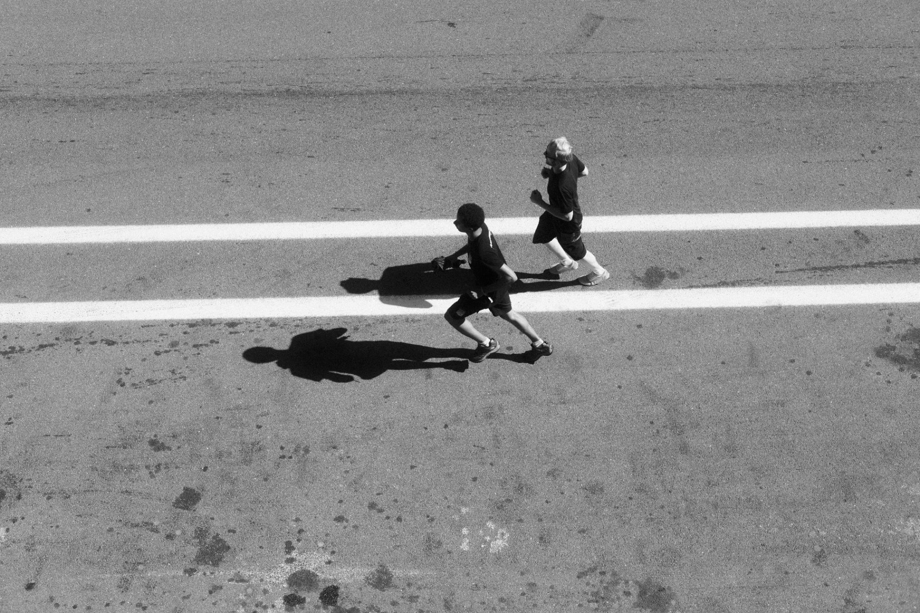 Two runners and their long shadows crossing pit straight lines