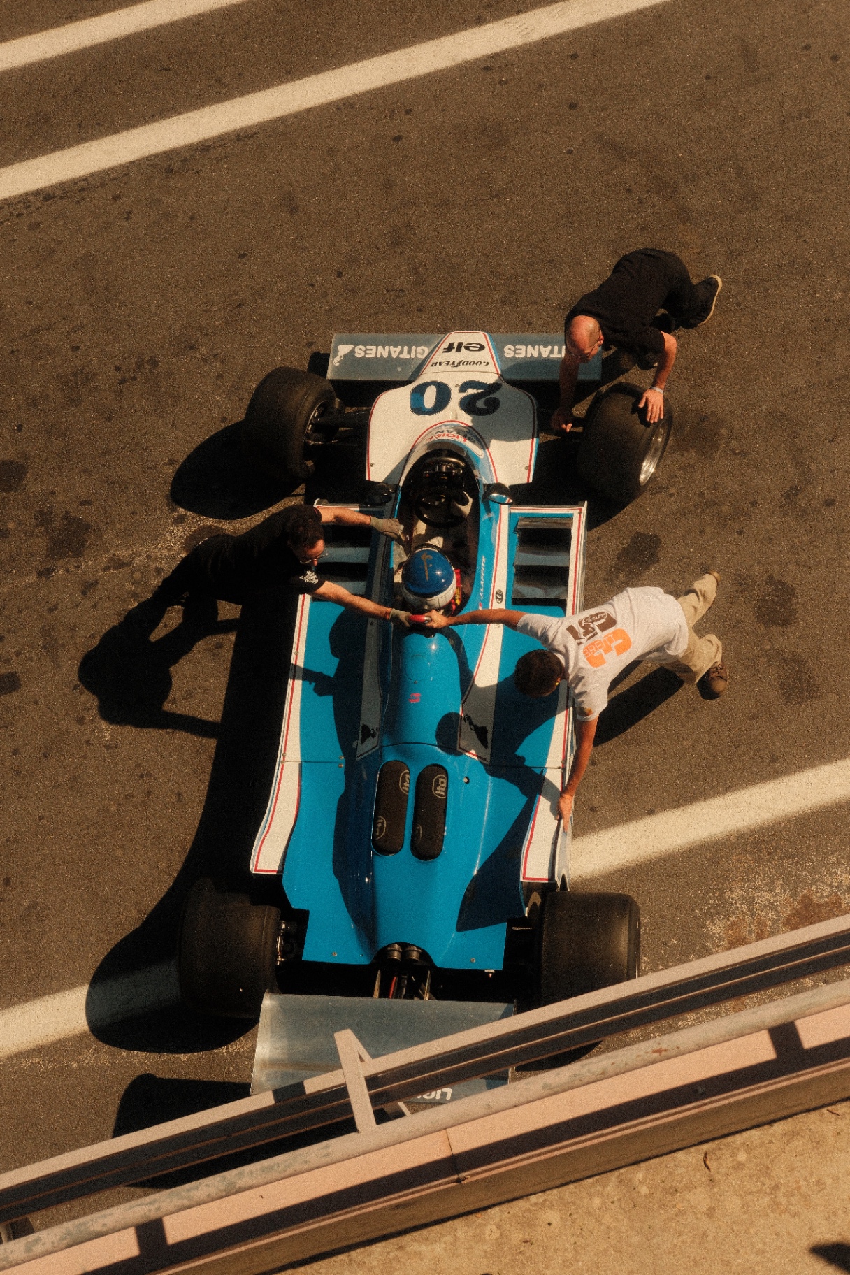 Overhead view of a blue vintage Formula car with crew in golden light