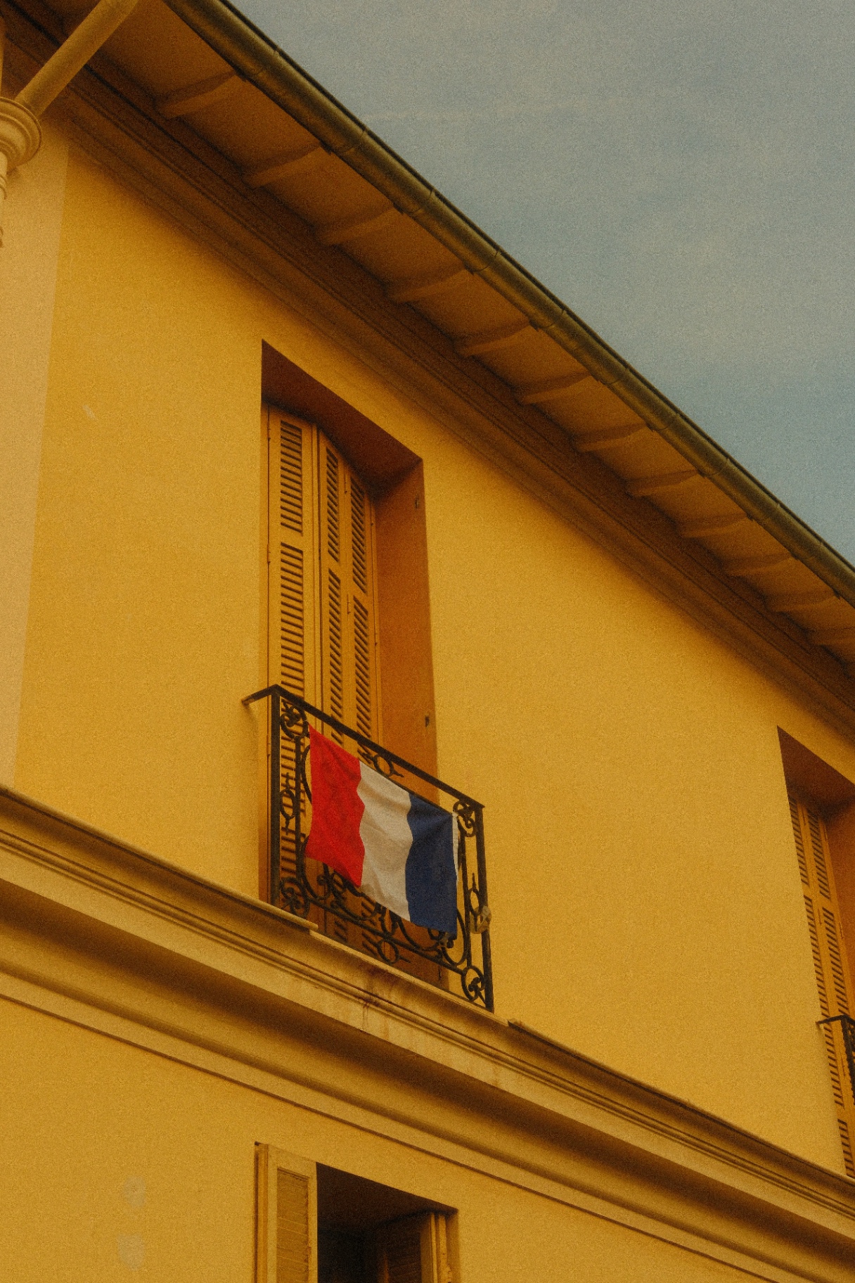 French flag on a wrought-iron balcony of a yellow facade