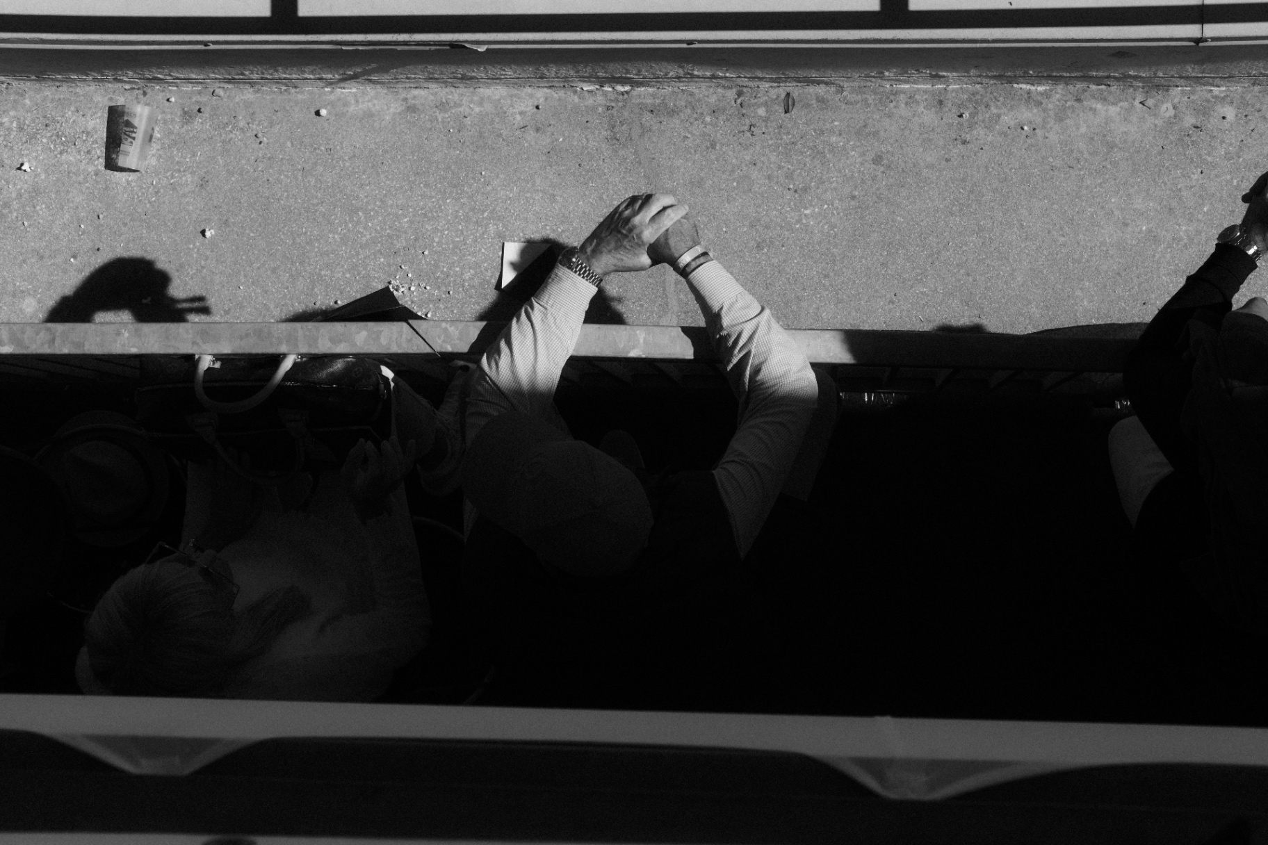 Overhead of a spectator clasping hands on a railing in hard light