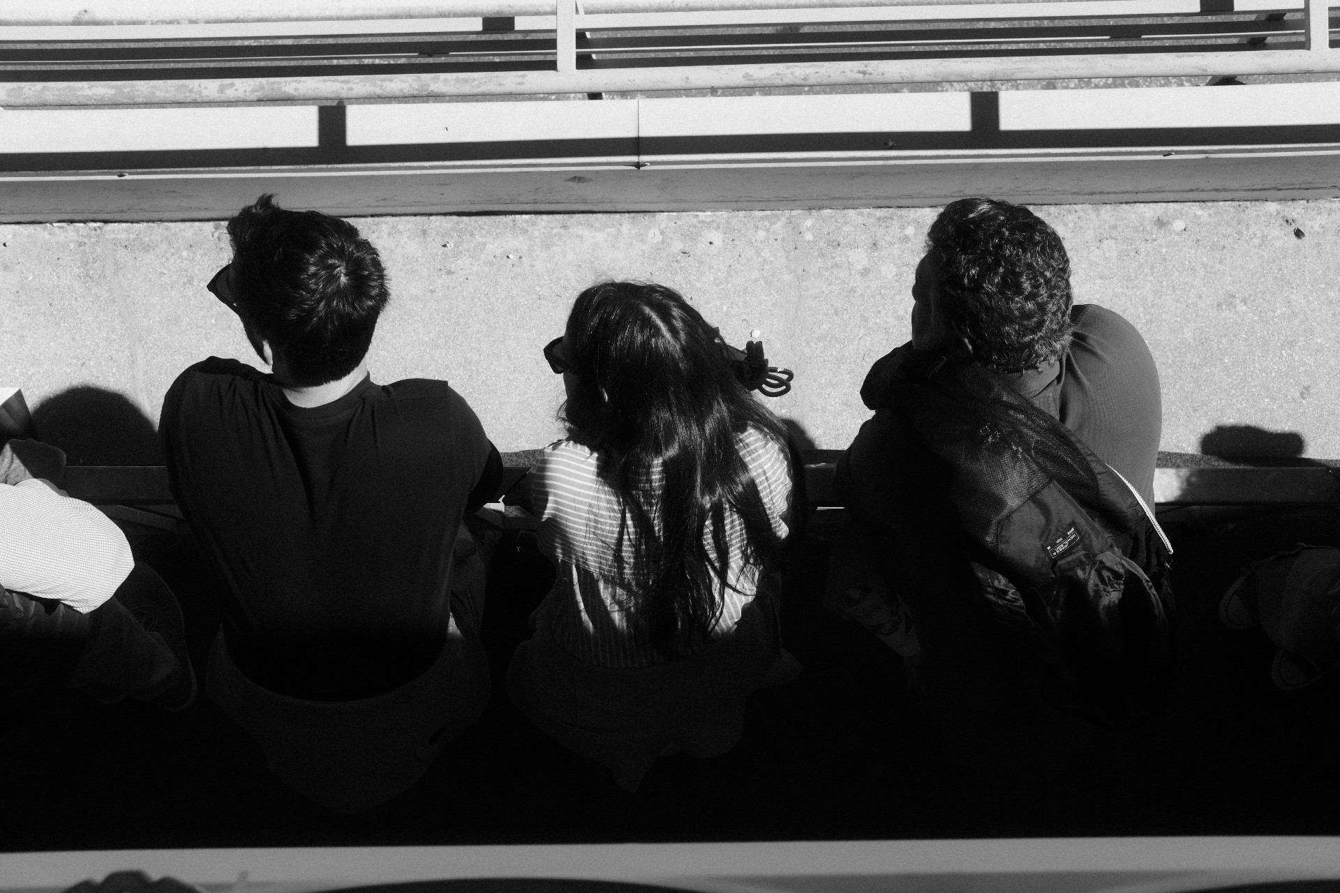 Three spectators leaning over a concrete trackside wall, black and white