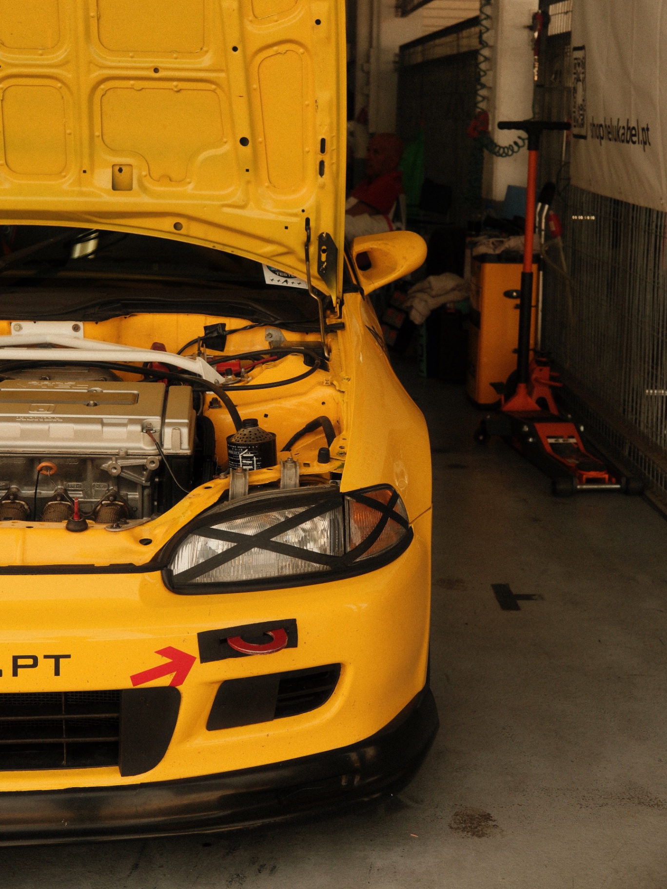 Yellow race-prepped Honda Civic with the hood up in a garage