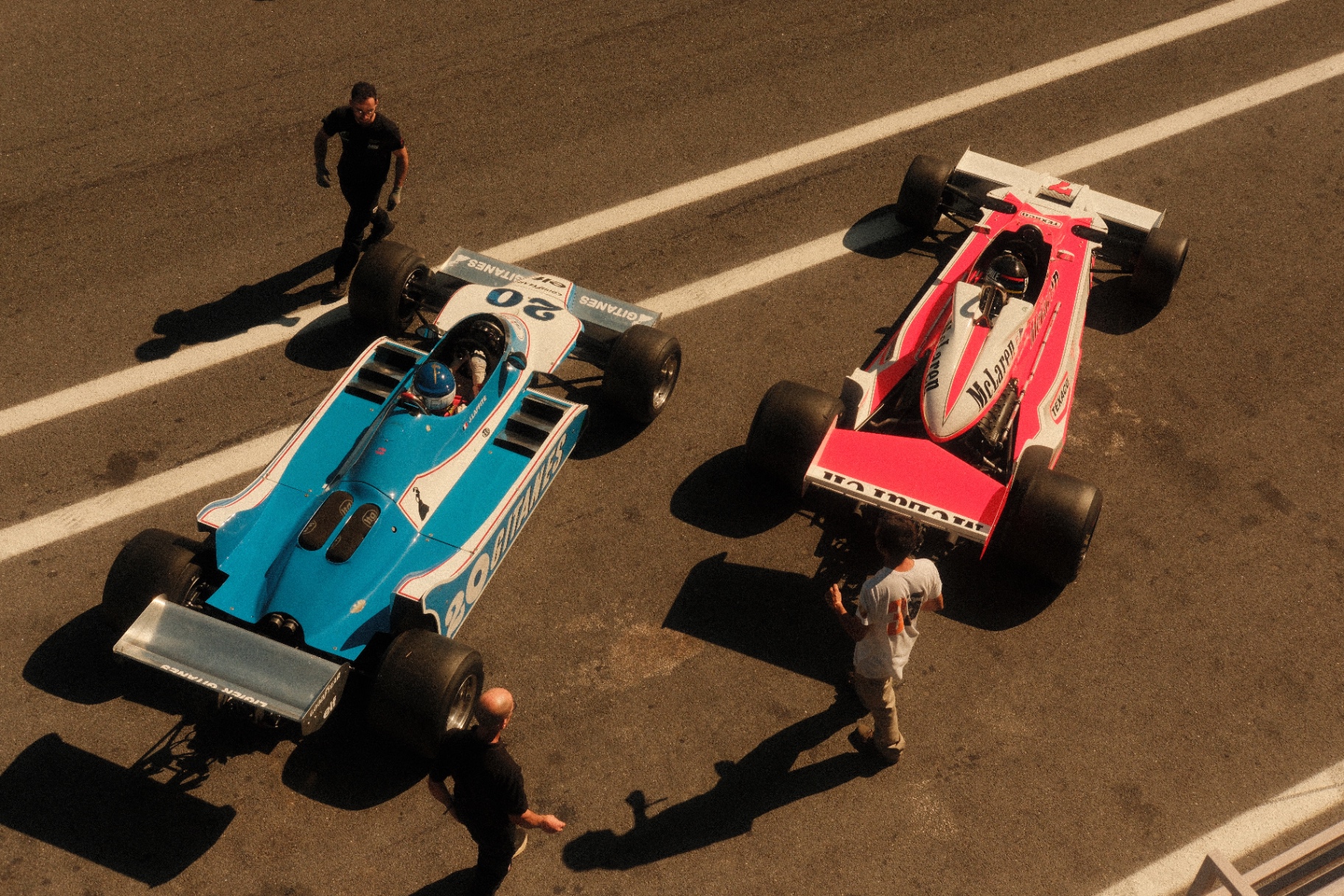 Two vintage Formula cars — blue Ligier and red McLaren — from above