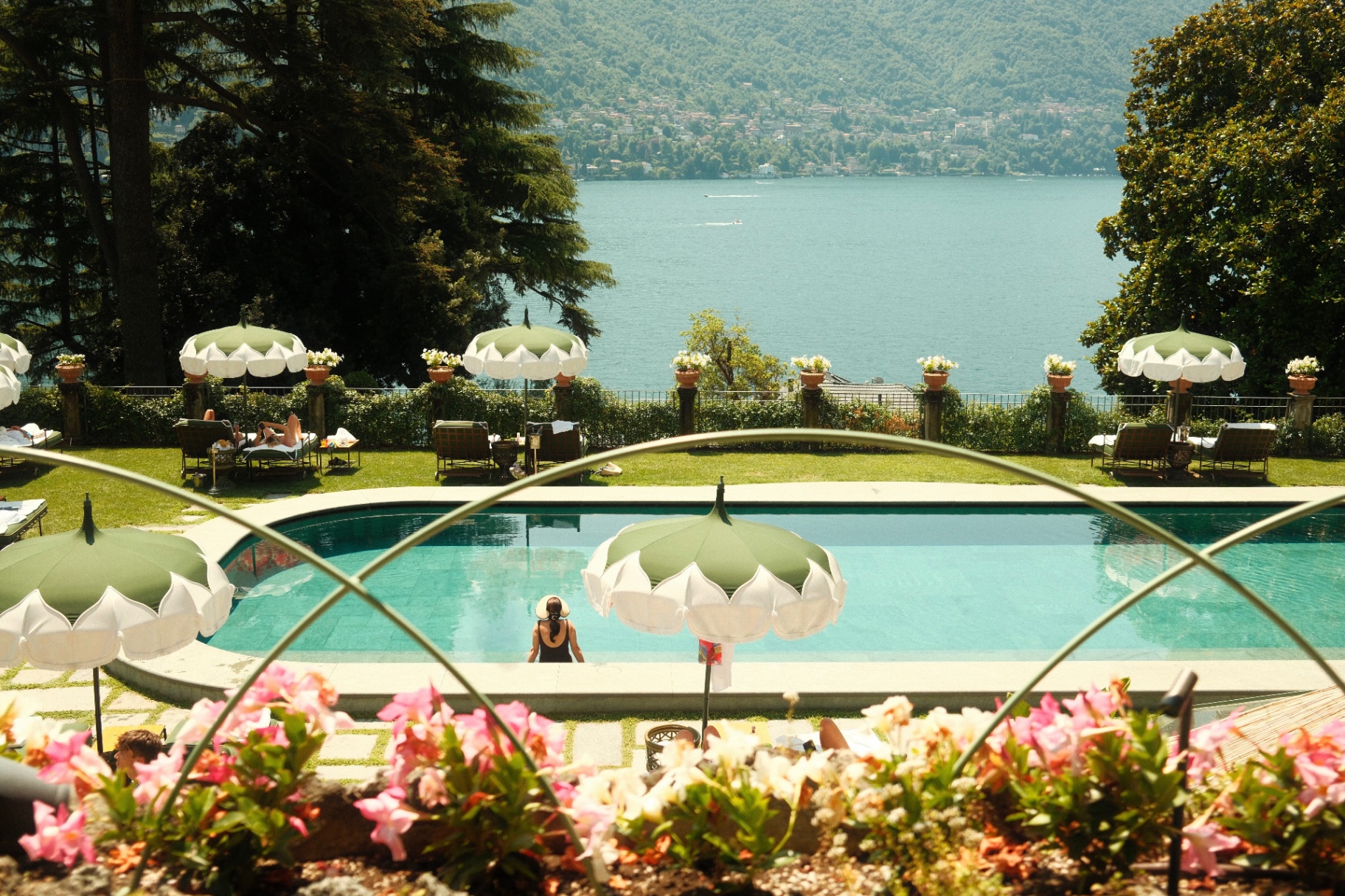 Pool and lake panorama at a Lake Como villa with green parasols and pink flowers