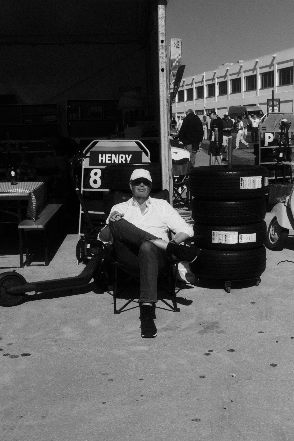 Man in white shirt seated beside stacked race tyres and a Henry pit board