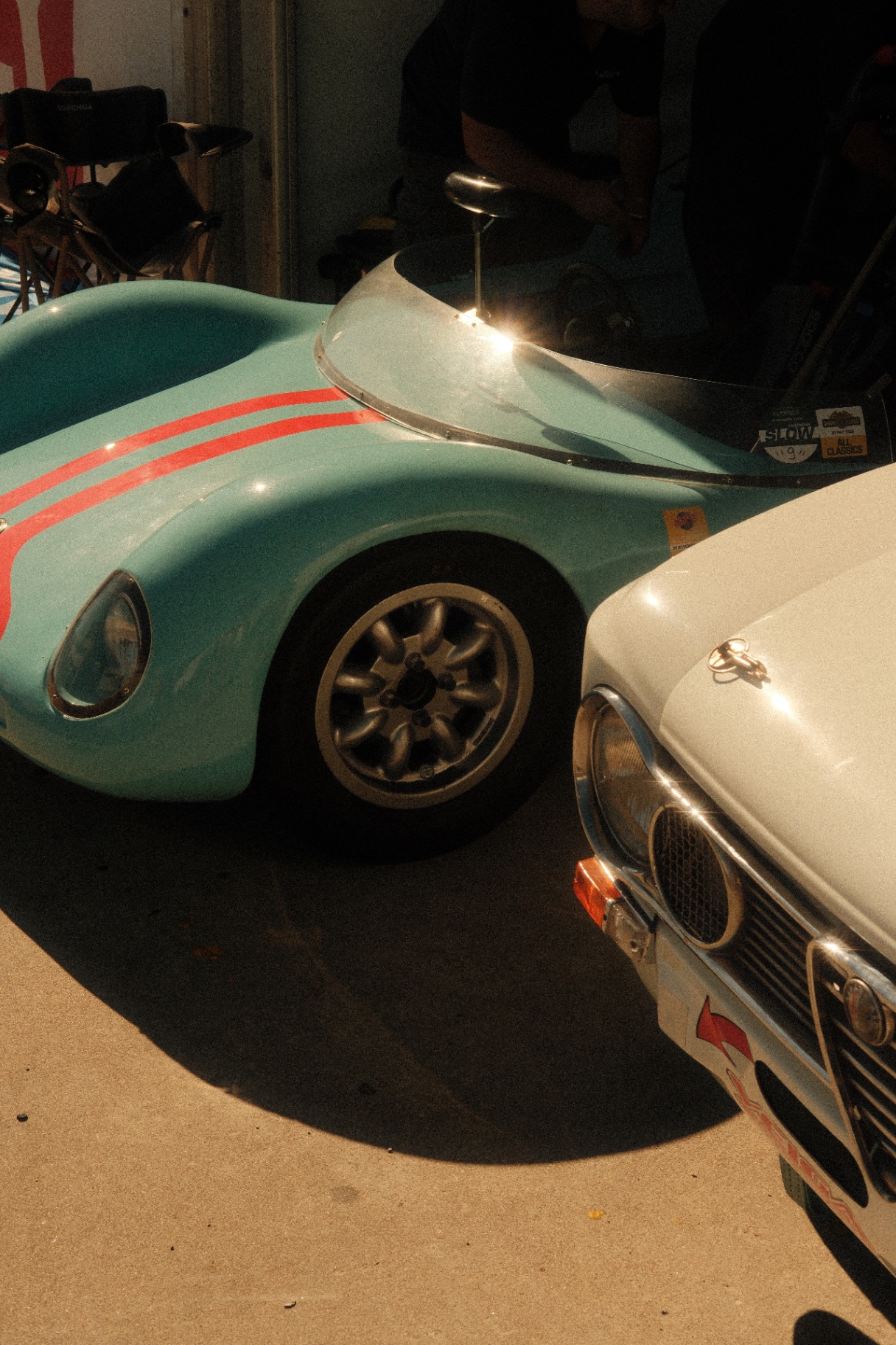Mint sports car with red stripes parked beside a white Alfa Romeo