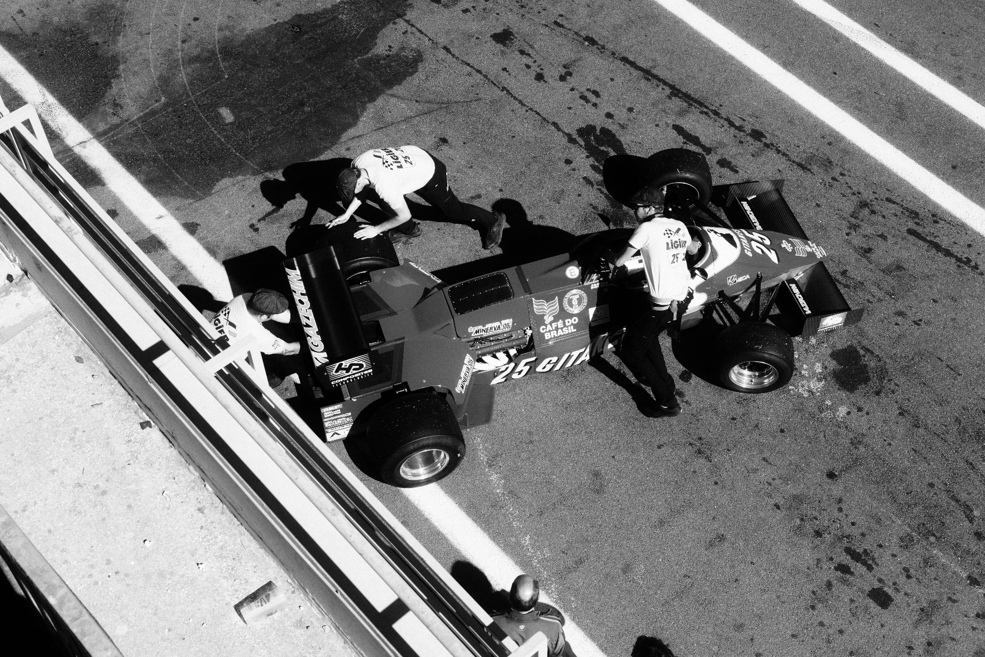 Black and white overhead of a Ligier being pushed in the pit lane
